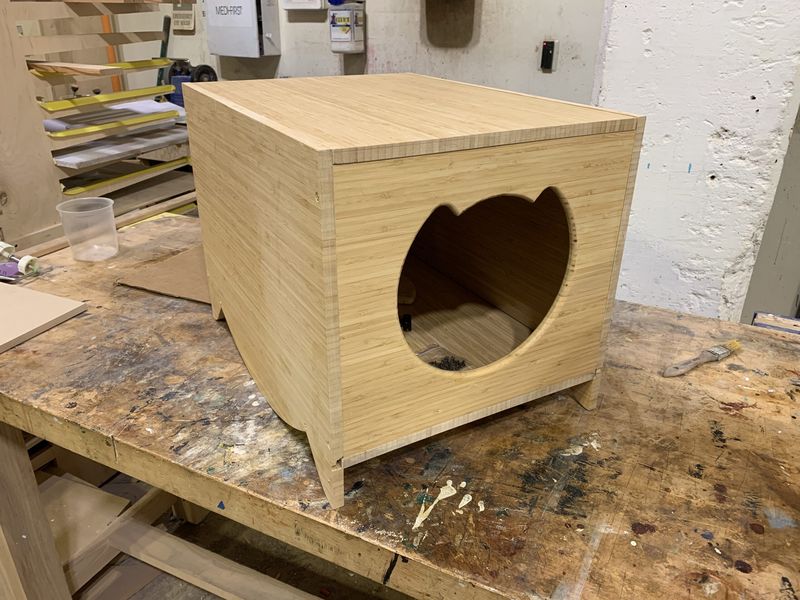 Bamboo litter box enclosure with a cat-shaped door, on a workbench